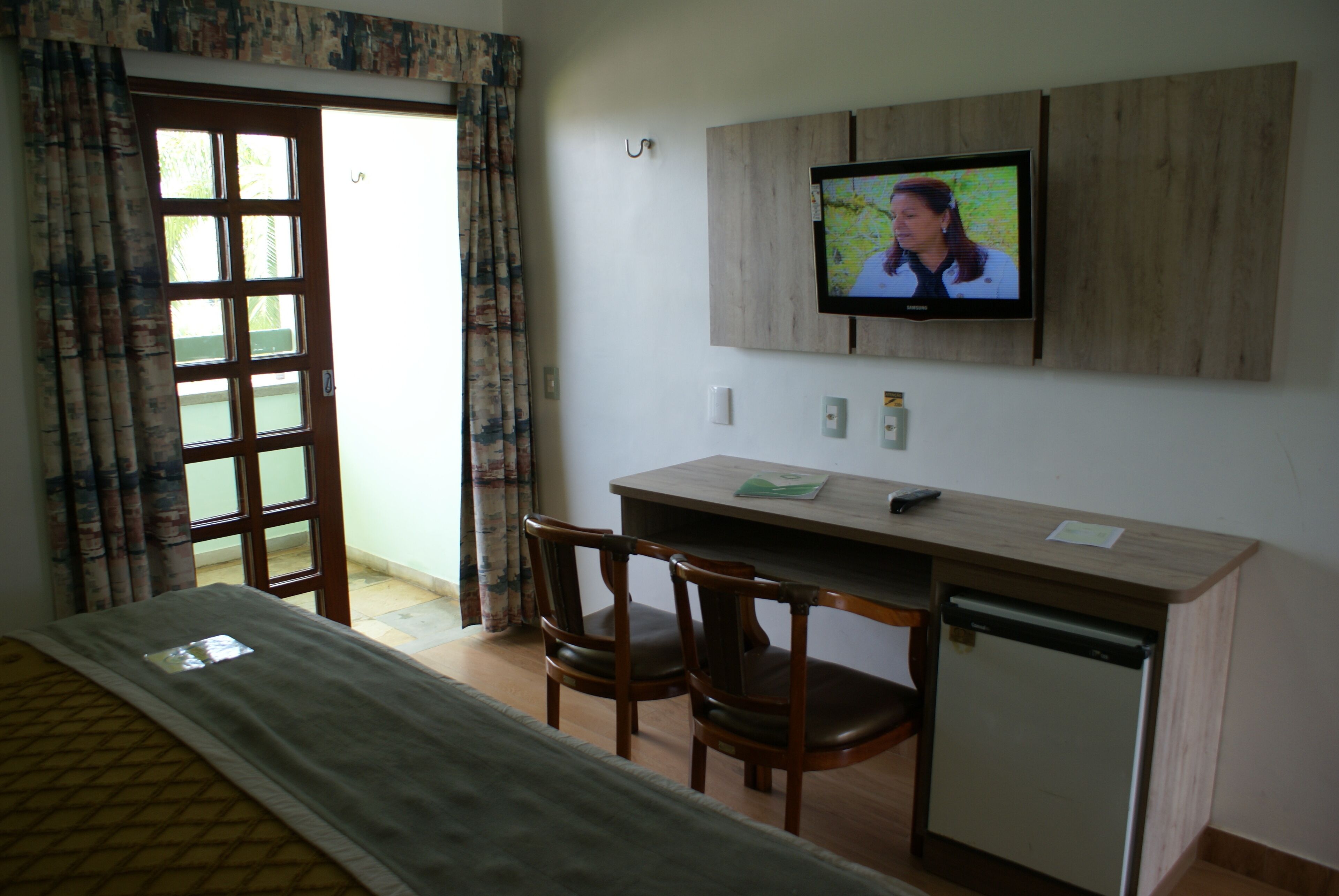 A hotel room with a bed, a desk with two chairs, a television, and a small refrigerator.