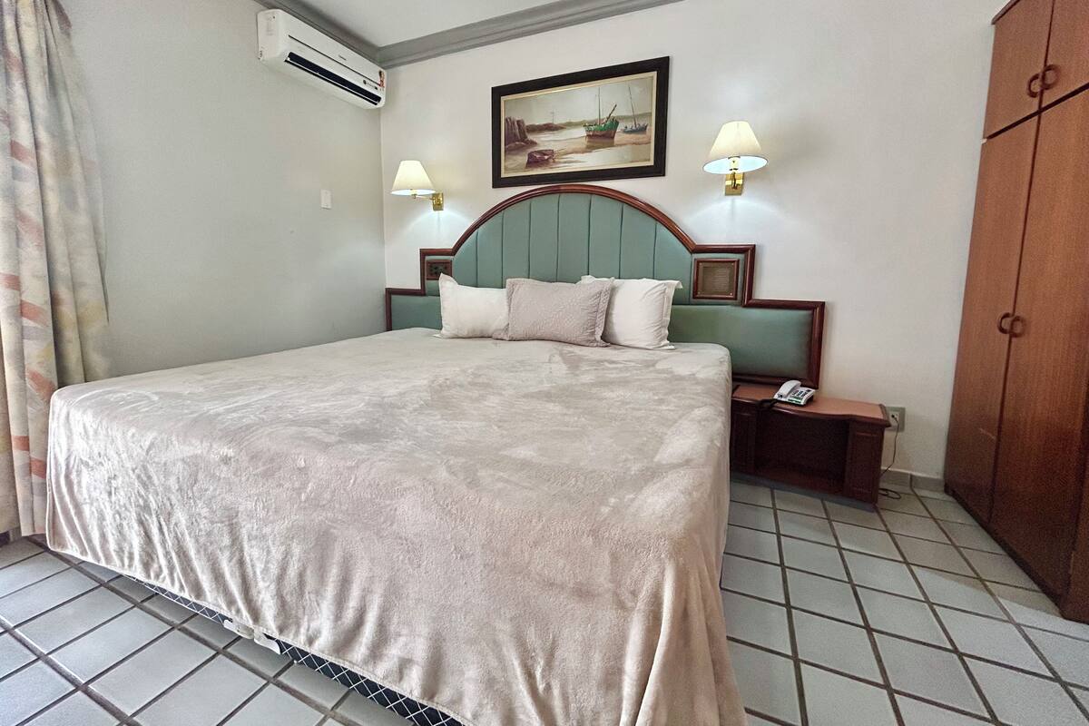 Habitación de hotel con cama, dos lámparas de noche, un cuadro, equipo de aire acondicionado, teléfono y armario.