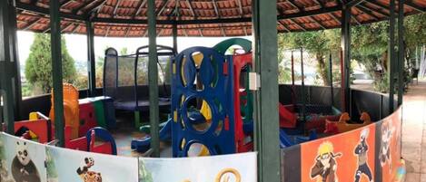 Ein Kinderspielbereich mit überdachter Konstruktion, bunten Spielgeräten und Wandgemälden von Zeichentrickfiguren.