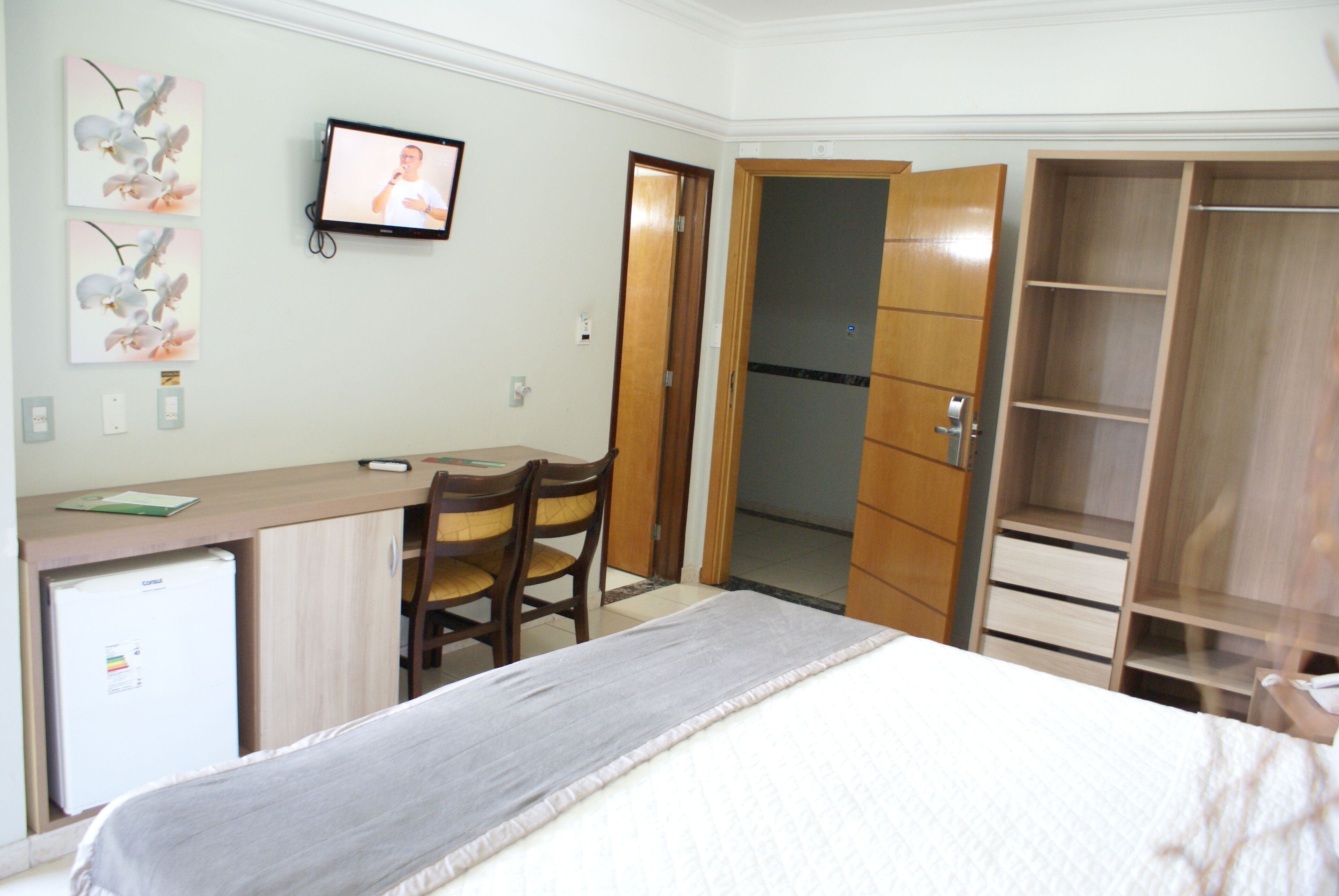 Una habitación de hotel con cama, escritorio, silla, televisor y armario.