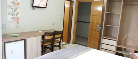 Una habitación de hotel con cama, escritorio, silla, televisor y armario.