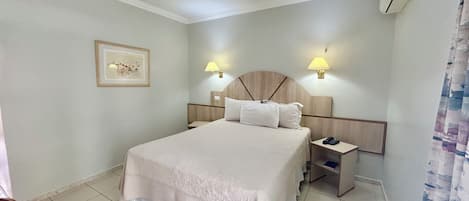 A hotel room with a large bed, two bedside tables, a wall-mounted lamp, a framed picture, and a ceiling light.