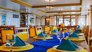 Een restaurant met een lange tafel gedekt voor diner, met blauwe servetten, gele tafelsetting en glazen.