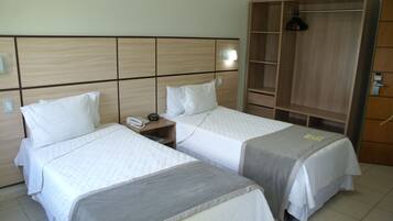 A hotel room with two beds, a wooden headboard, a wardrobe, and a bedside table with a telephone.