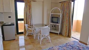 A room with a bed, a small table with chairs, a television, and a balcony with curtains.