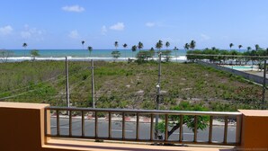 Blick vom Balkon auf einen Strand mit Palmen und blauem Himmel.