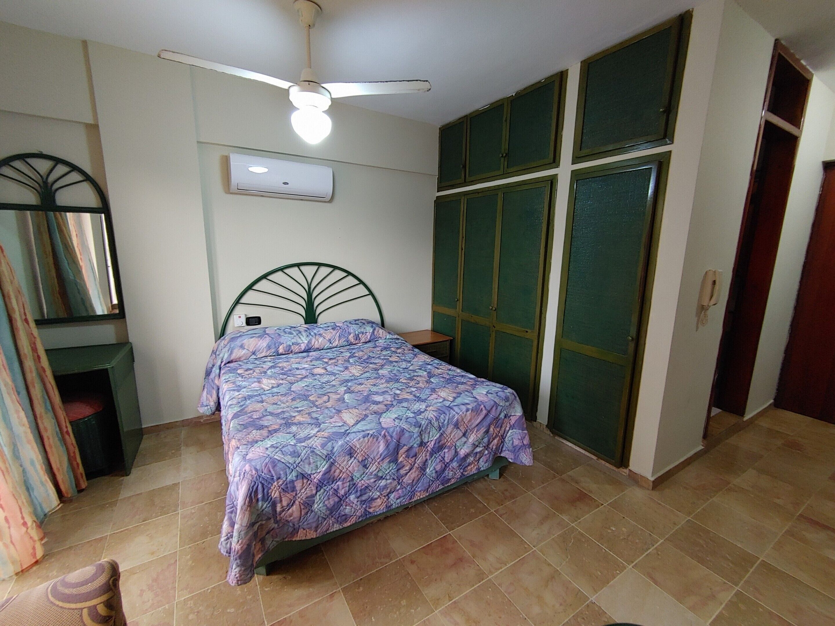 Un dormitorio con cama, ventilador de techo, armario, espejo y teléfono.