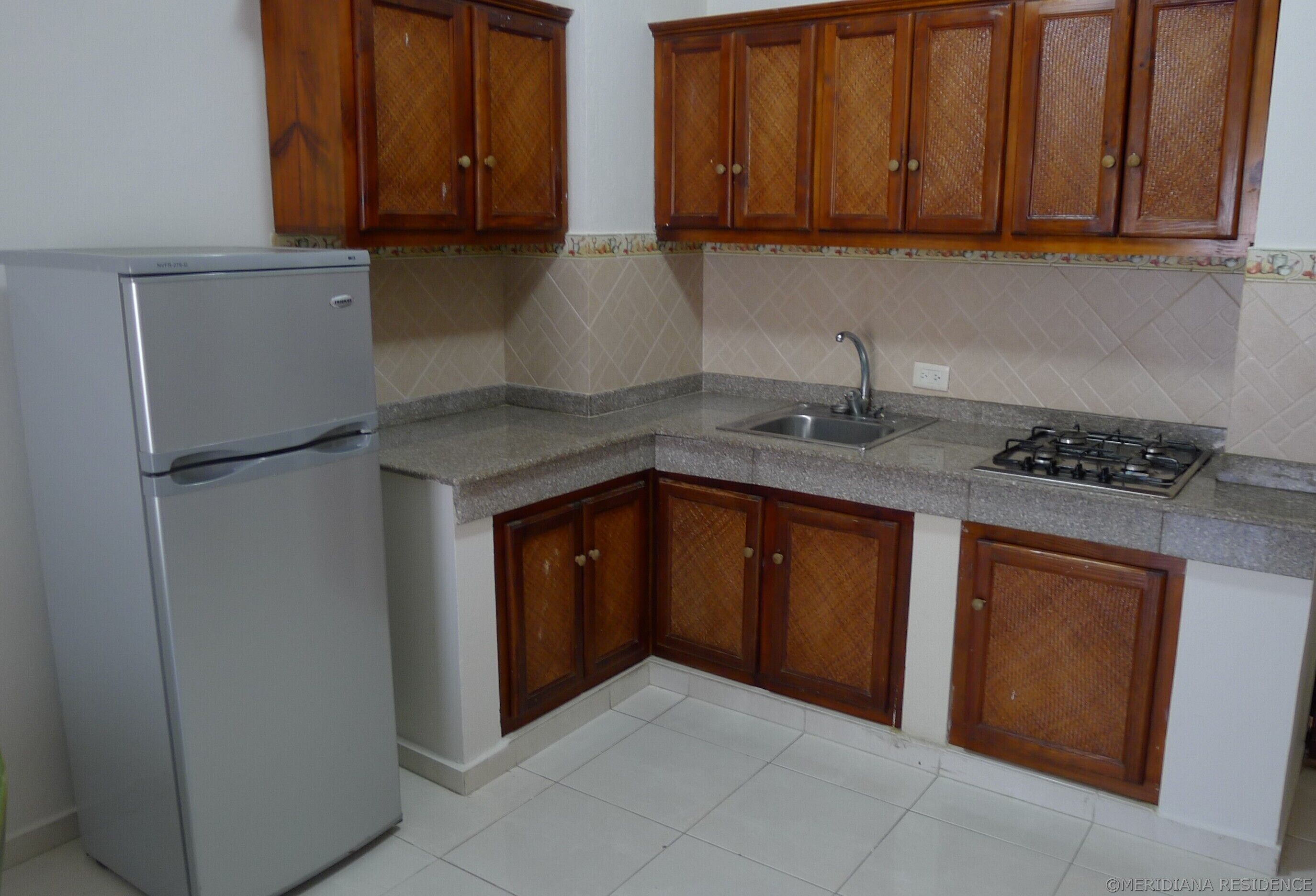 A kitchen with wooden cabinets, a stainless steel refrigerator, a sink, and a gas stove.
