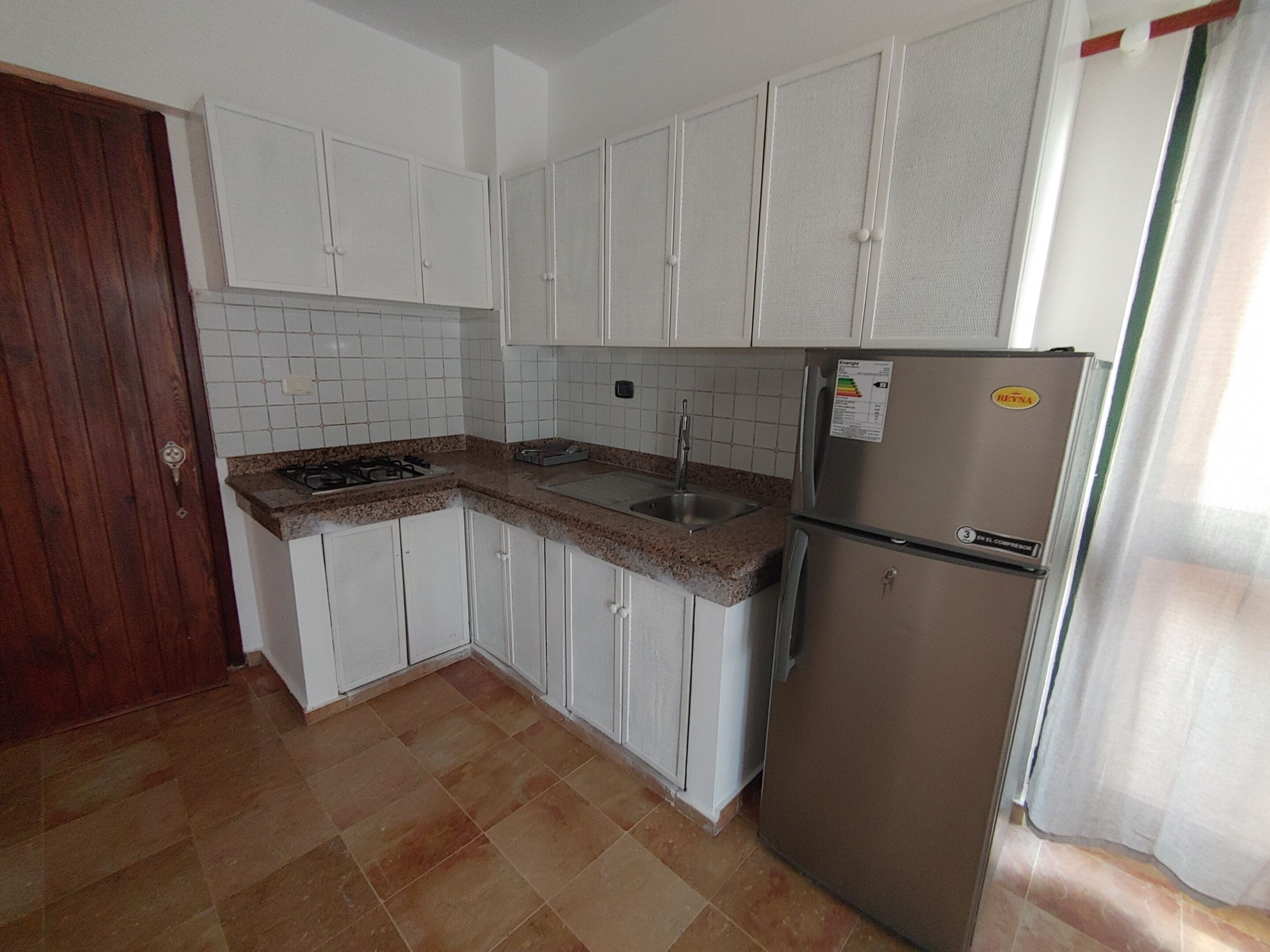 A kitchen with white cabinets, a stainless steel refrigerator, a gas stove, and a sink.