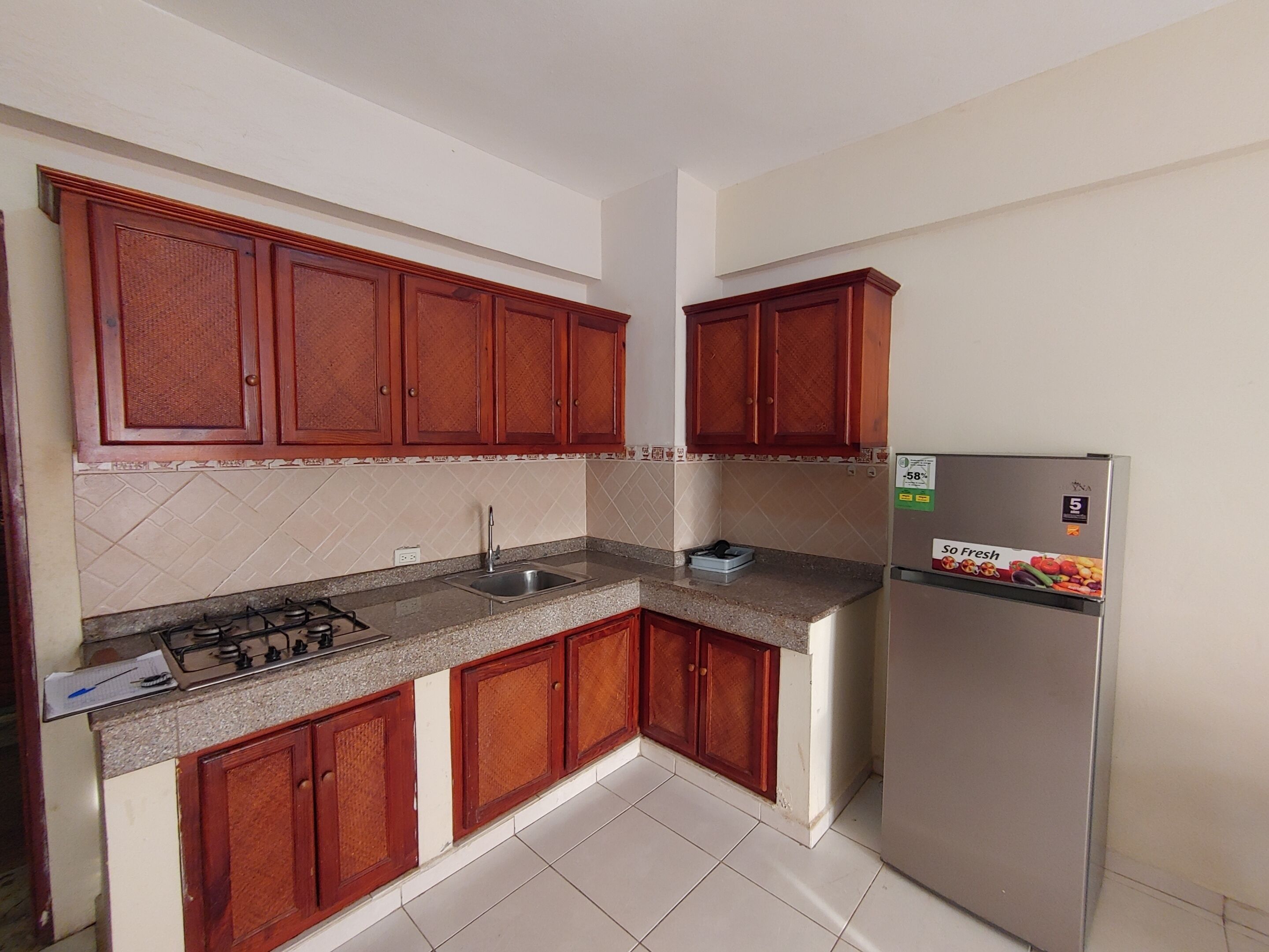 A compact kitchen with wooden cabinets, a stainless steel refrigerator, and a gas stove.