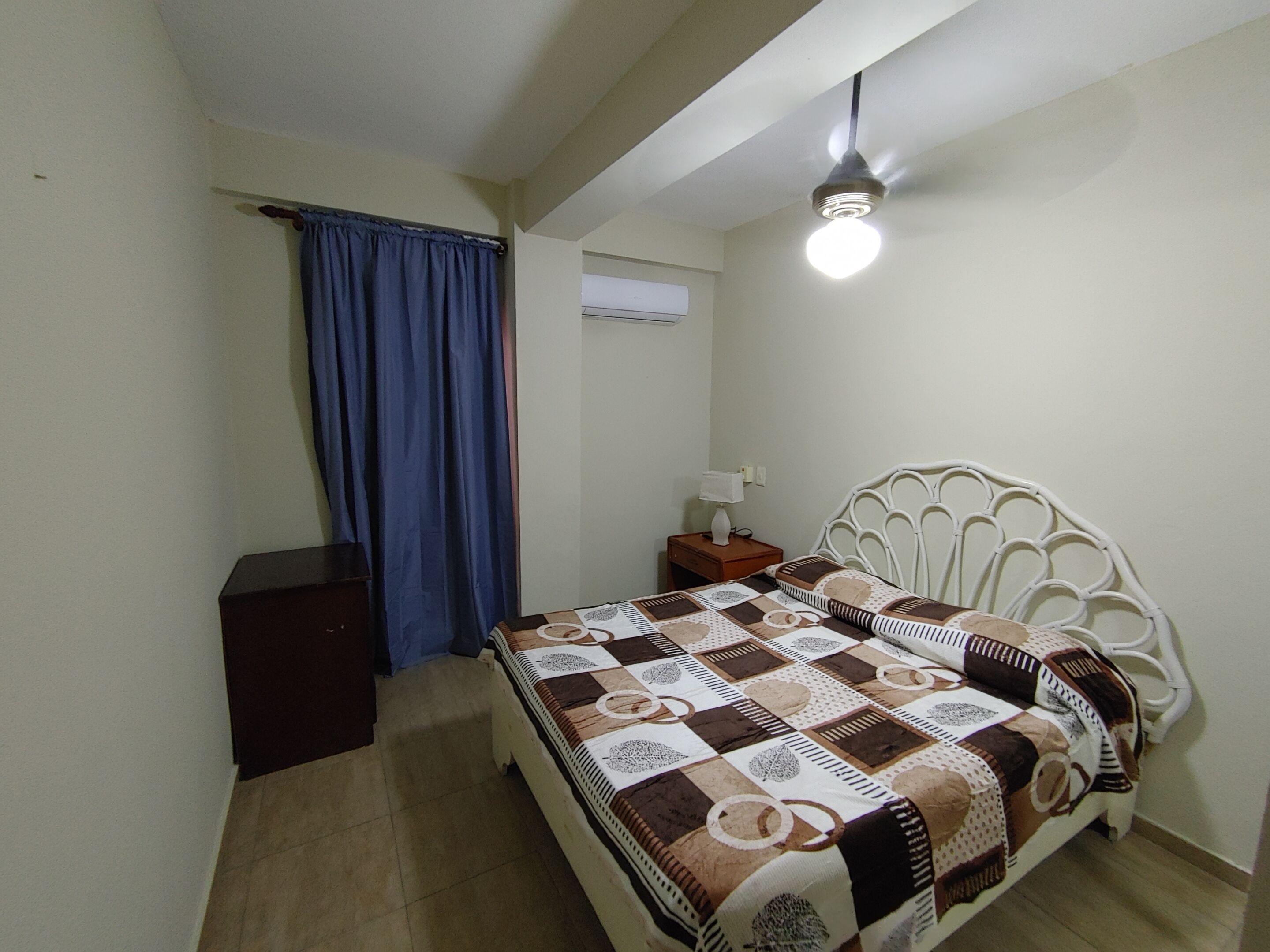 A bedroom with a bed, a nightstand, a lamp, a ceiling fan, and a window with curtains.