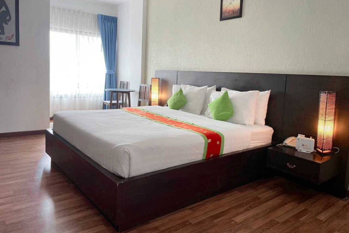 A hotel room with a large bed, a nightstand with a lamp, a window with curtains, and a picture on the wall.