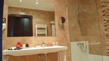A modern bathroom with a large mirror, a shower, and a sink with toiletries.