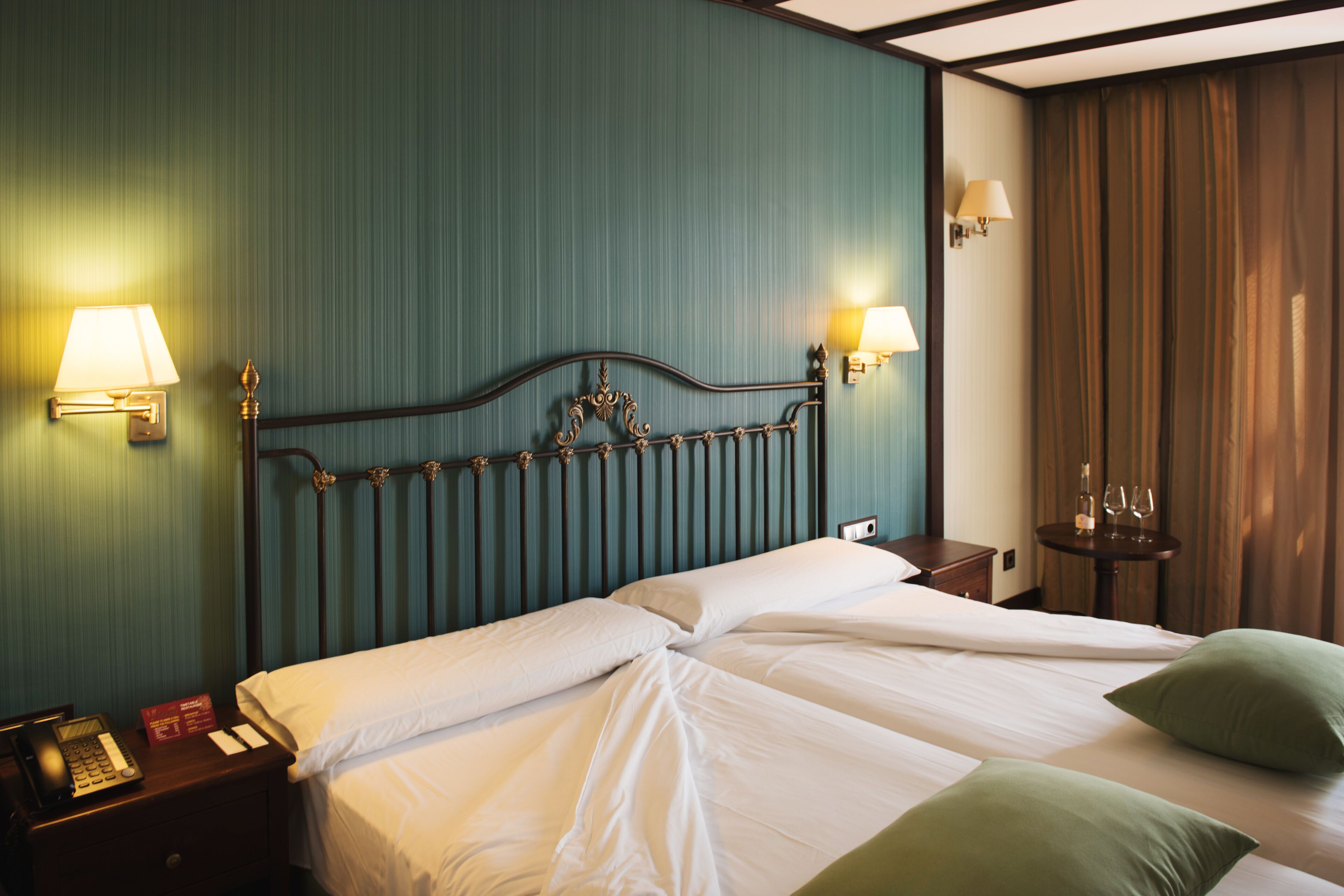 Una habitación de hotel con dos camas, una mesita de noche con teléfono y lámparas de pared.