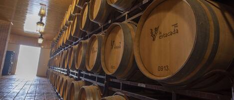 Wooden wine barrels stacked in rows inside a building with a tiled floor and hanging lights.