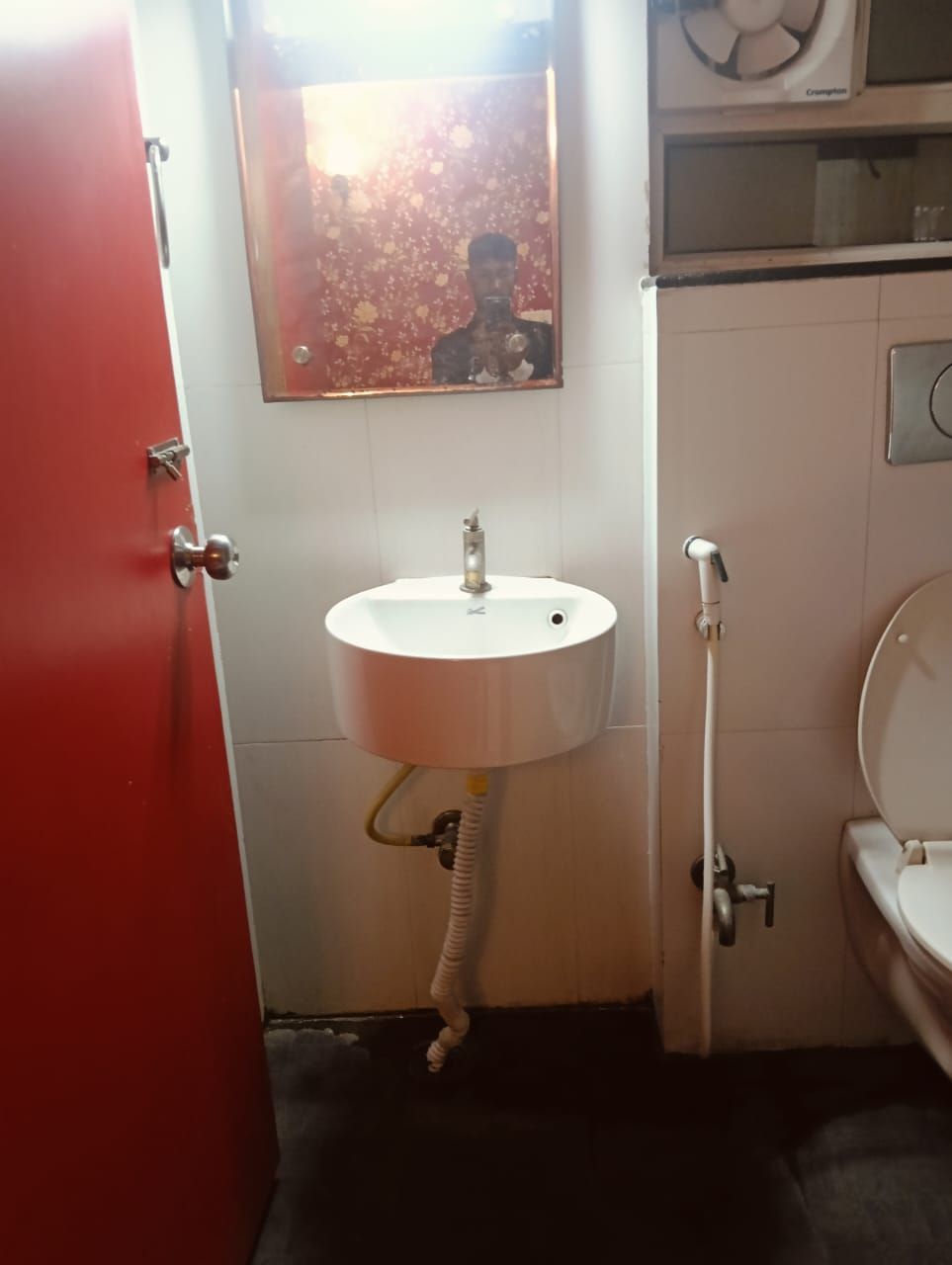 A bathroom with a white sink, a mirror, a toilet, and a red door.