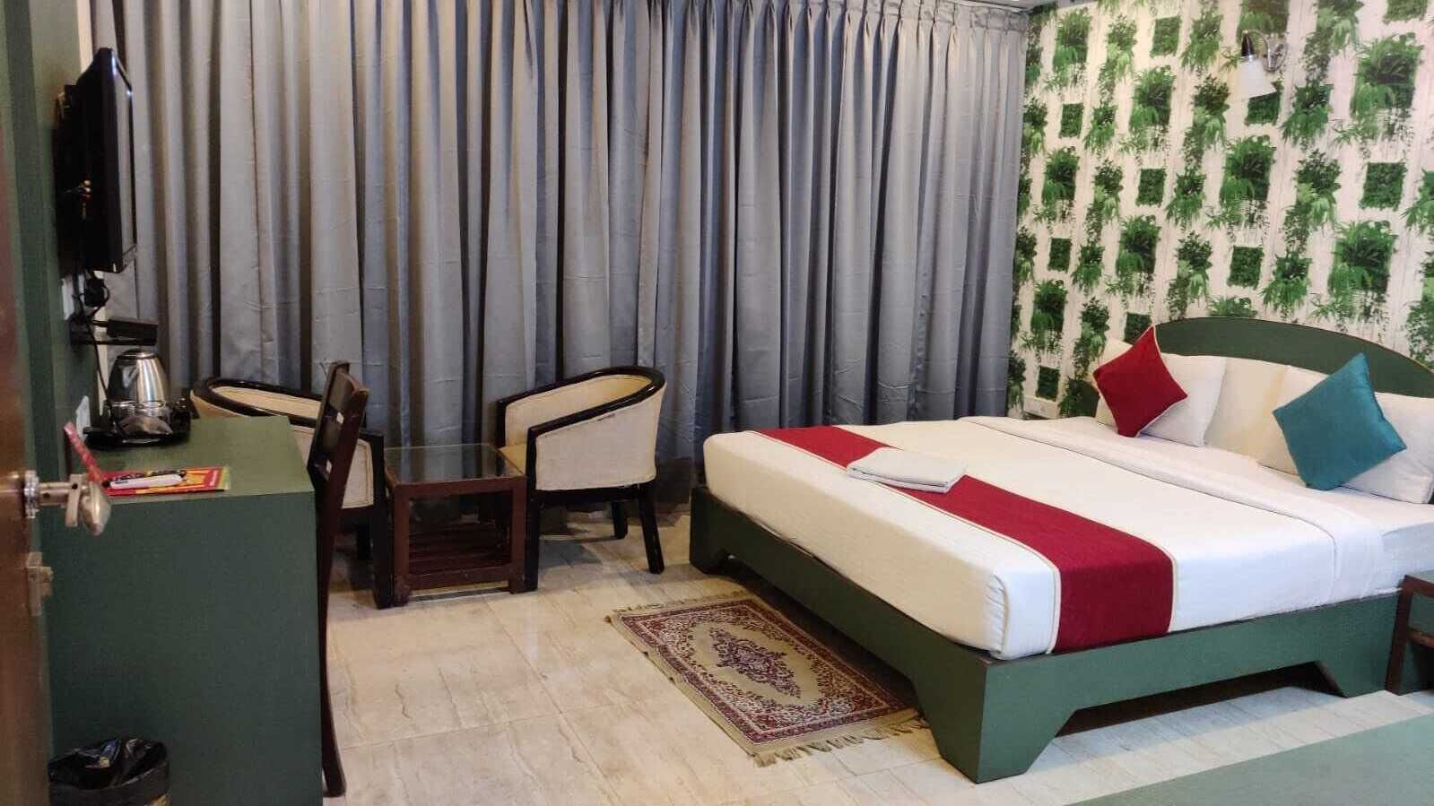 Une chambre d’hôtel avec un lit, un bureau, deux chaises, une machine à café et un mur décoré de motifs.