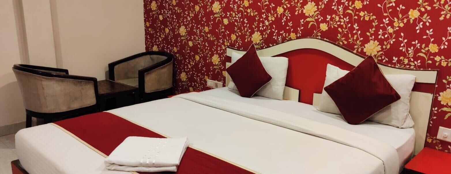 A hotel room with a bed, two chairs, a red and white bedspread, and a floral wallpaper.