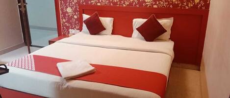 Una cama con cabecera roja, ropa de cama blanca y almohadas rojas.