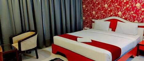 Habitación de hotel con cama, una silla, una mesita de noche y papel tapiz floral rojo.