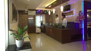 A reception area with a wooden reception desk, a potted plant, and a seating area with a sofa and chair. - Royal Shades (Bengaluru)
