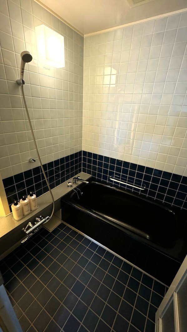 A bathroom with a black bathtub, a shower, and a sink with toiletries.