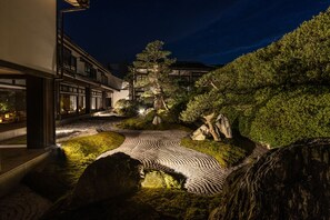 A nighttime view of a traditional Japanese garden with a winding stone path, a large tree, and a building with illuminated windows. - Hagi No Yado Tomoe (Hagi)