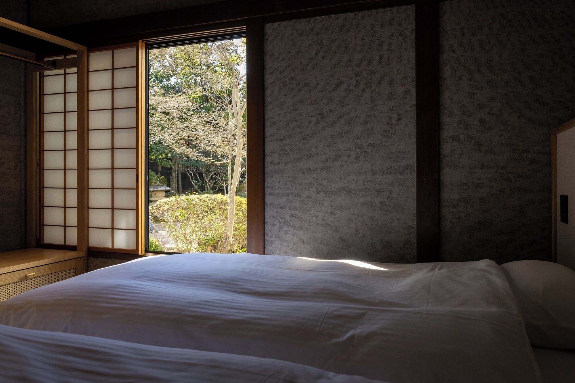 Una habitación japonesa tradicional con suelo de tatami, una cama baja y una puerta corrediza que da a un jardín.