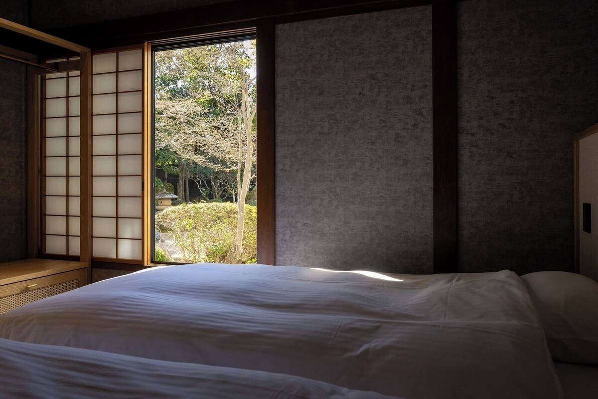 A traditional Japanese room with tatami flooring, a low bed, and a sliding door leading to a garden.