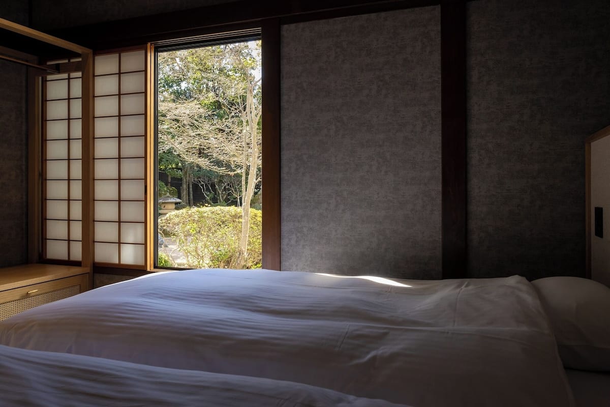 Una habitación japonesa tradicional con suelo de tatami, una cama baja y una puerta corrediza que da a un jardín.