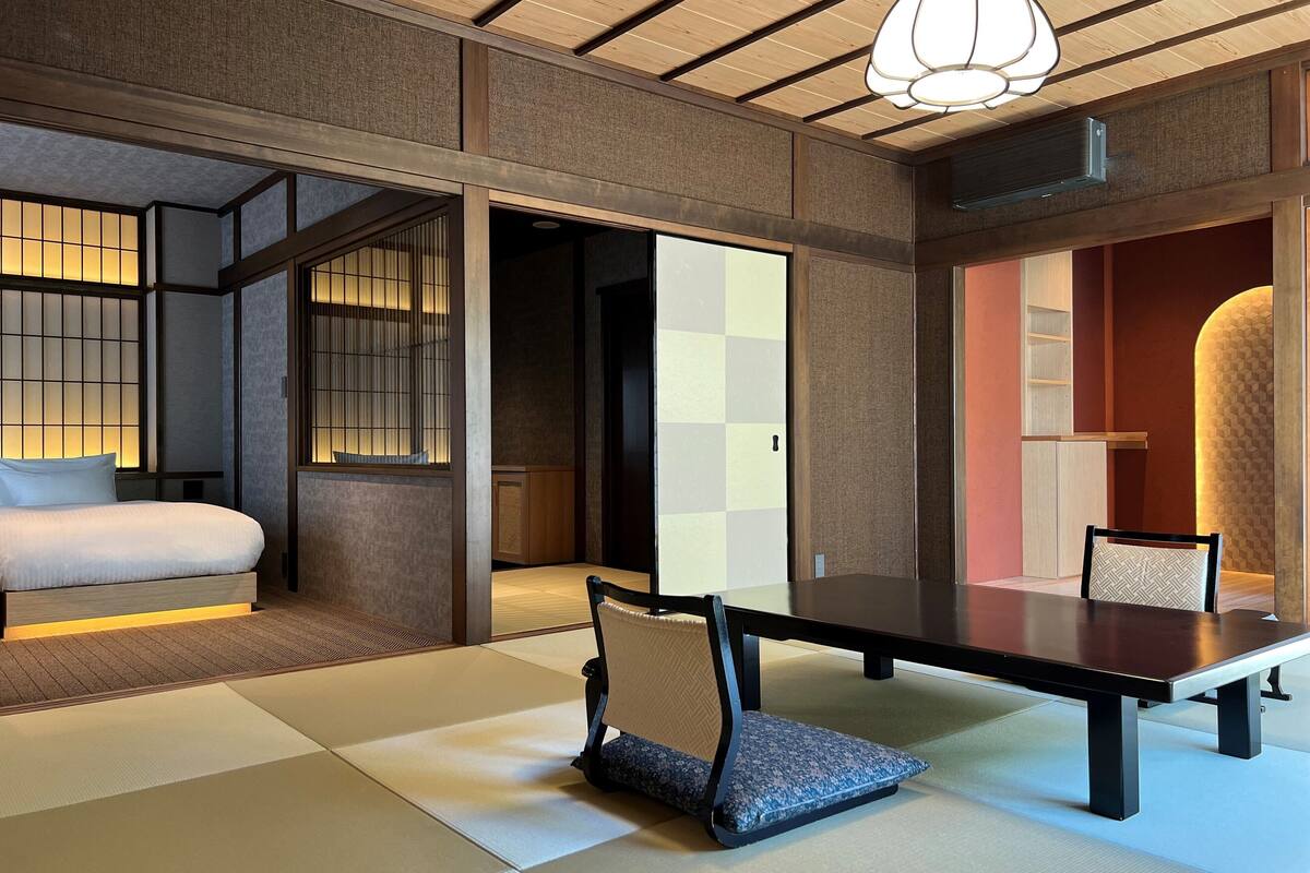 A traditional Japanese-style room with tatami flooring, a low table, and a bed with a futon.