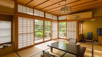 A traditional Japanese room with tatami flooring, a low table, a cushioned chair, sliding shoji doors, and a view of a garden.