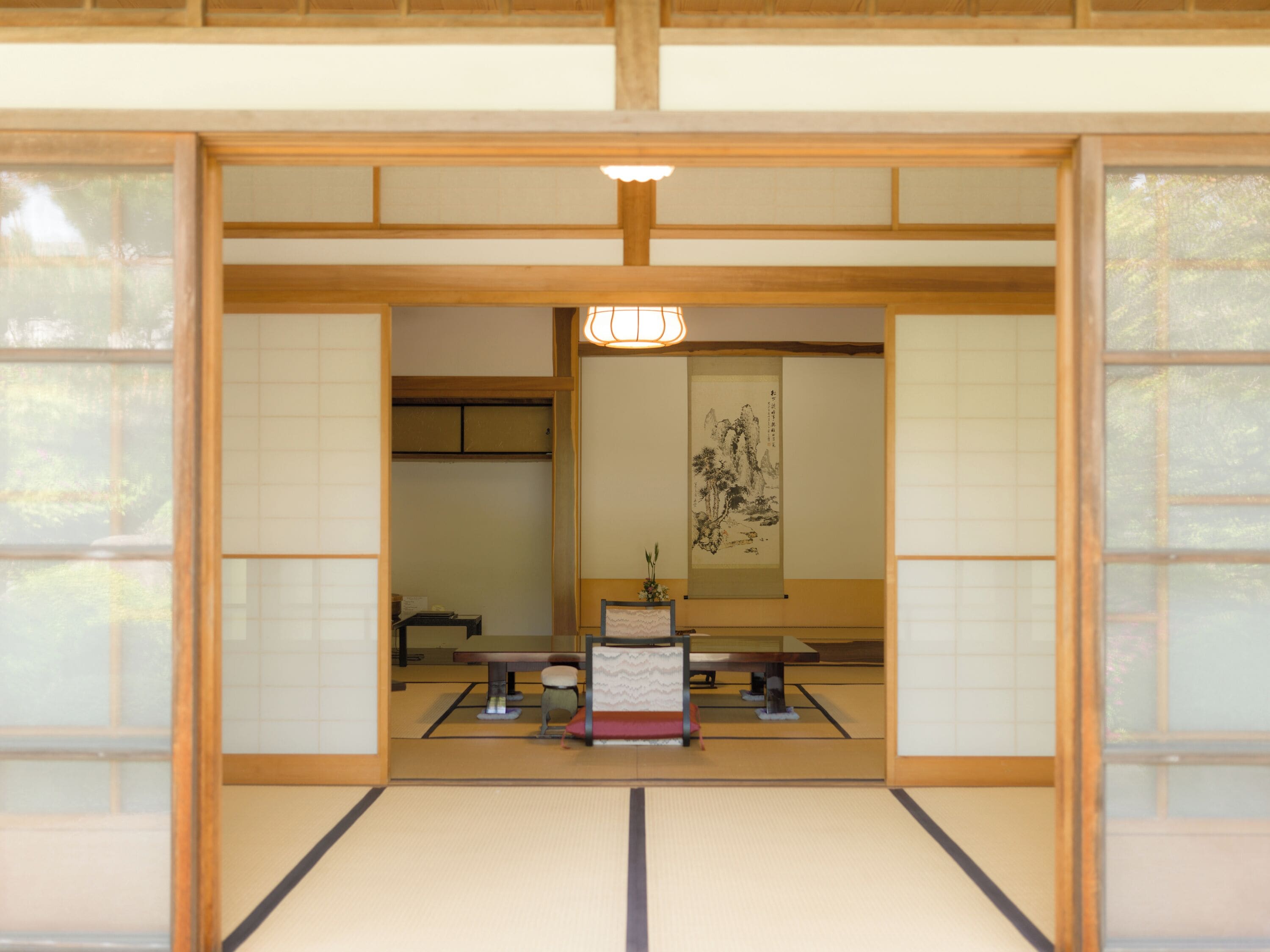 A traditional Japanese room with tatami flooring, a shoji screen door, a tatami mat table, and a hanging scroll.