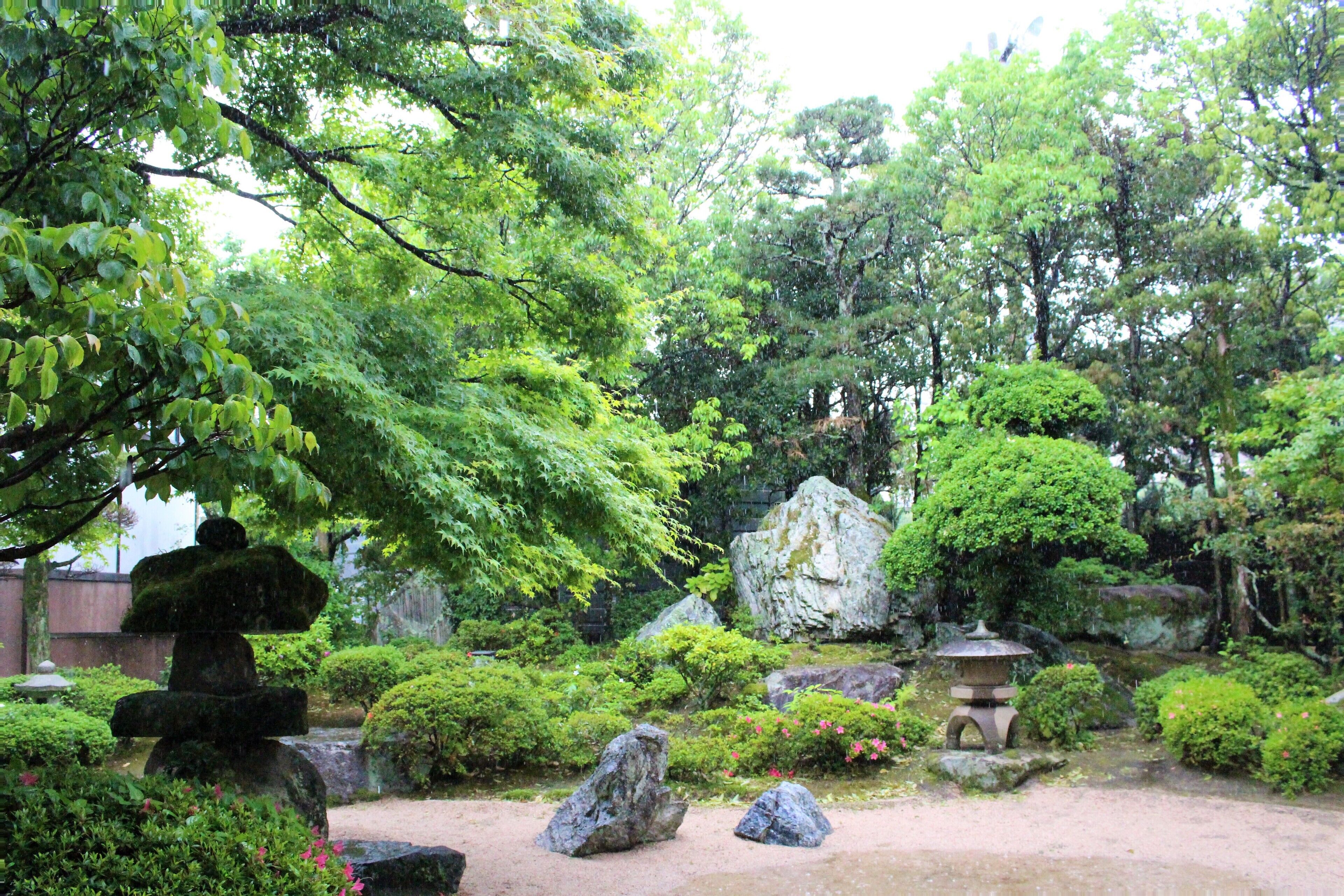 A traditional Japanese garden with rock formations, a stone lantern, and lush greenery.