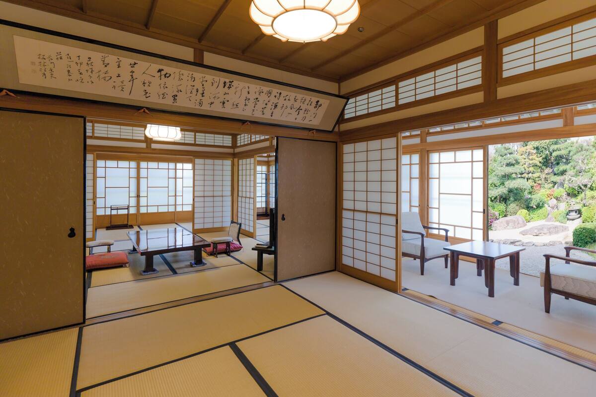 A traditional Japanese room with tatami flooring, sliding doors, and a view of a garden.