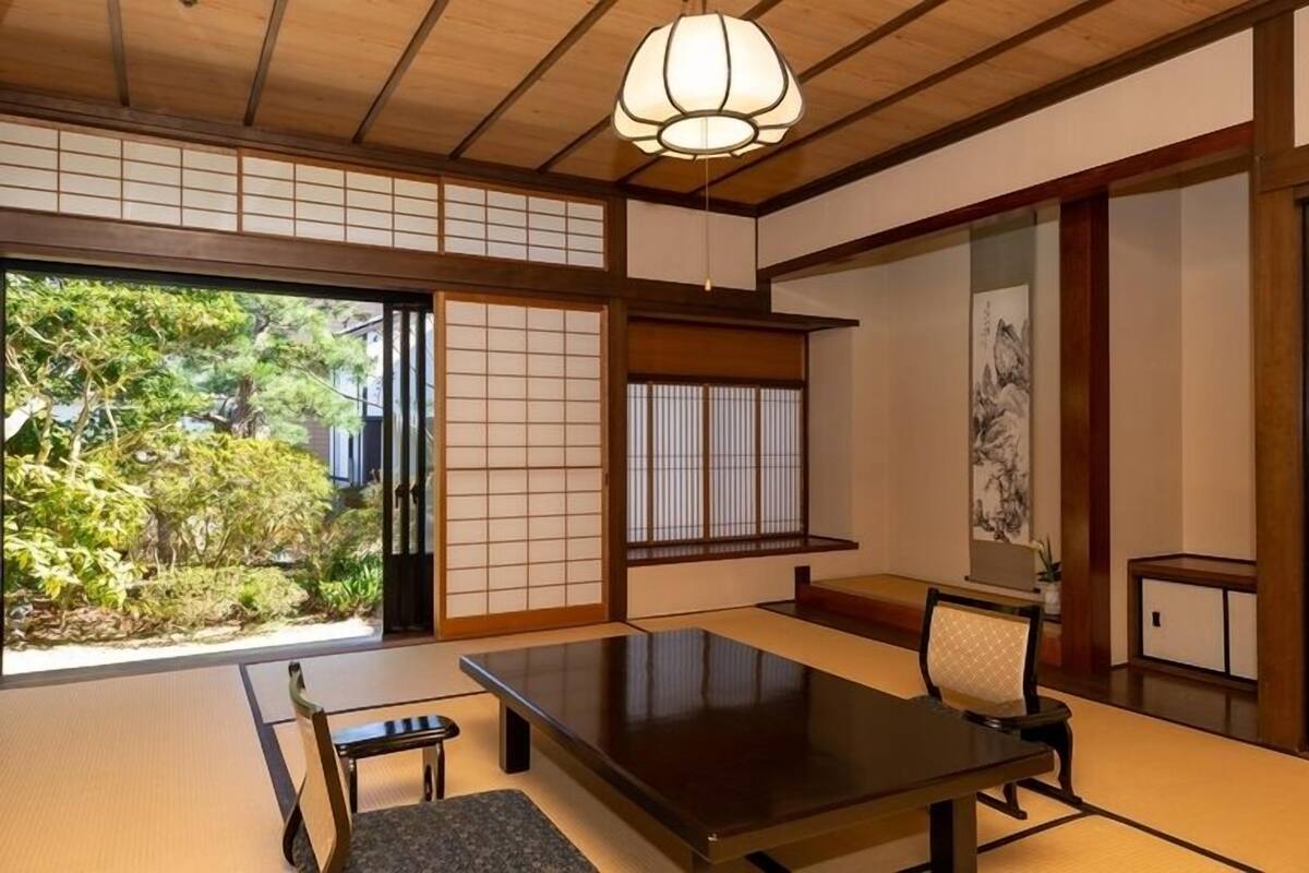 A traditional Japanese room with tatami flooring, a low table, a chair, sliding doors, and a hanging light fixture.
