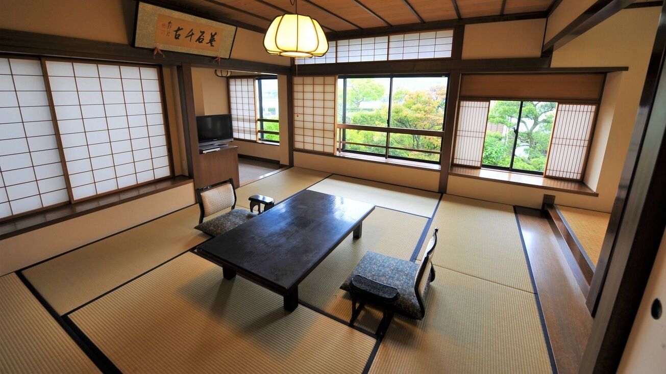 Una habitación con tatami, una mesa baja, bancos, un televisor y puertas correderas.