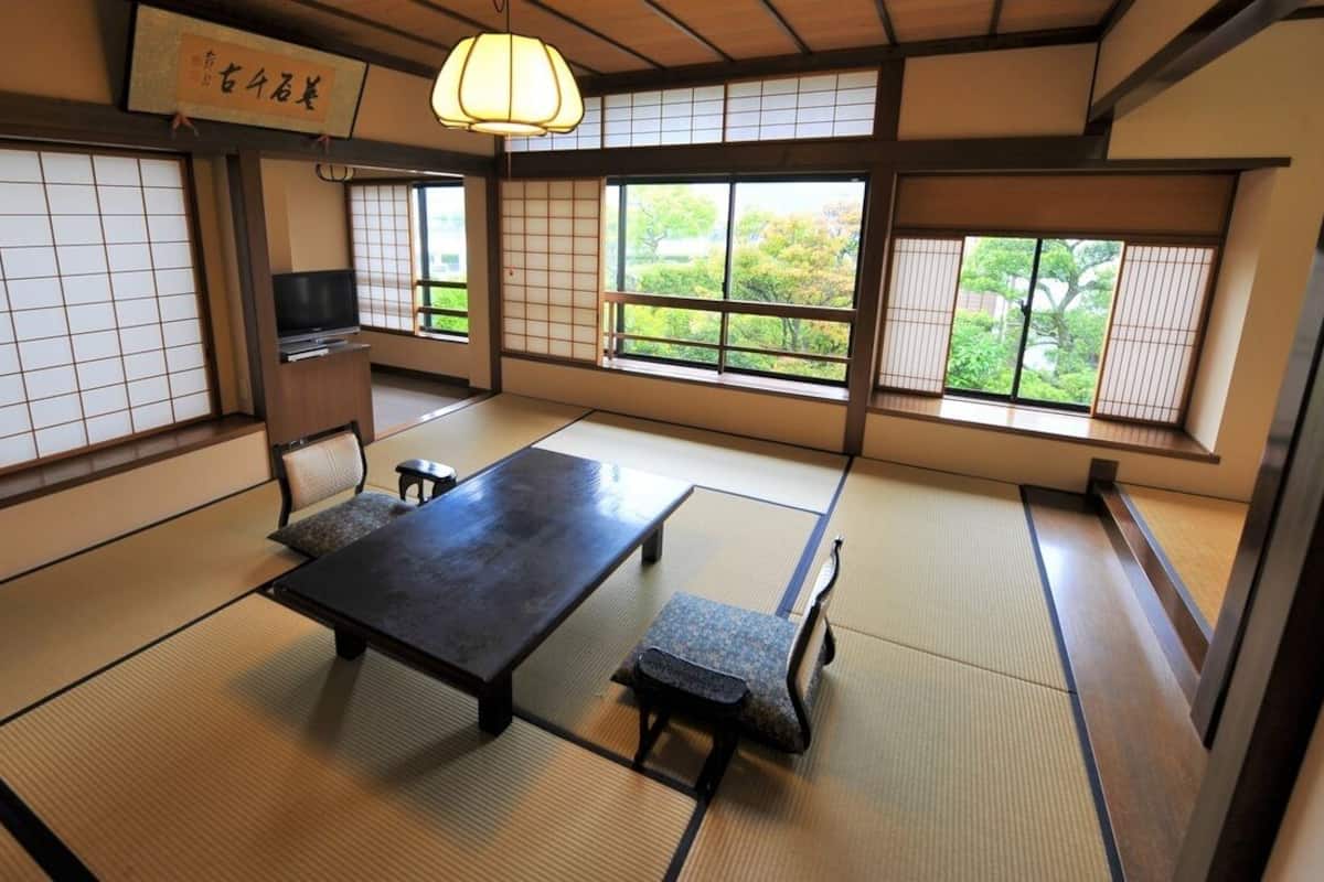 Una habitación con tatami, una mesa baja, bancos, un televisor y puertas correderas.