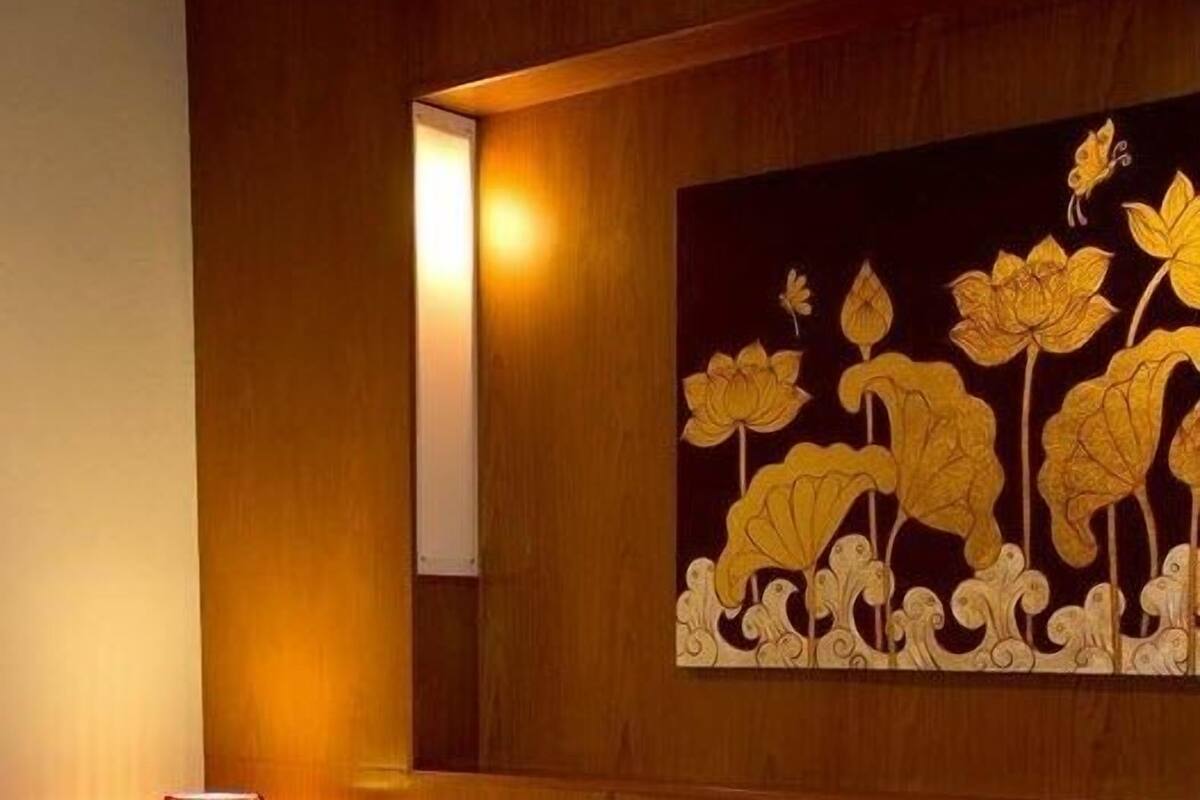 A hotel room with a bed, pillows, a wall painting, and a lamp.