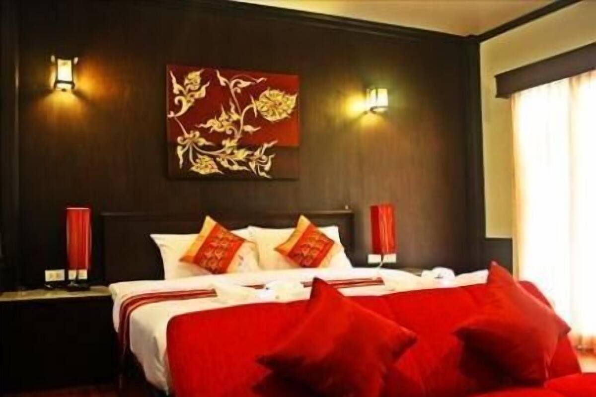 A hotel room with a large bed, red bedding, and a decorative wall piece.