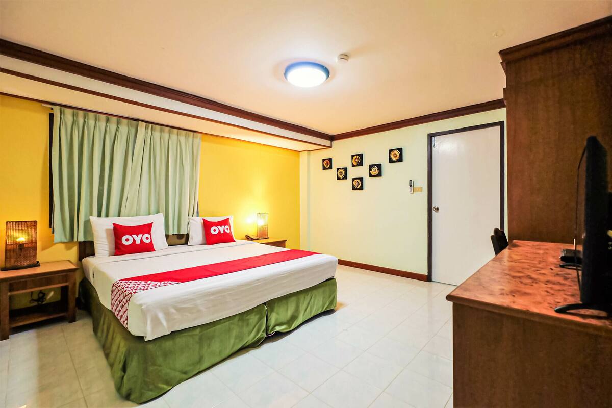 A hotel room with a bed, a desk, a nightstand, a door, and a wall with framed pictures.