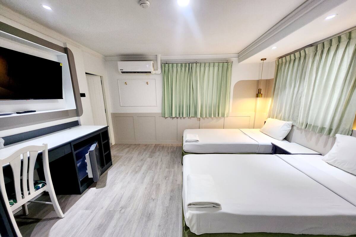 A hotel room with a TV, air conditioning, two beds, a desk, and a chair.