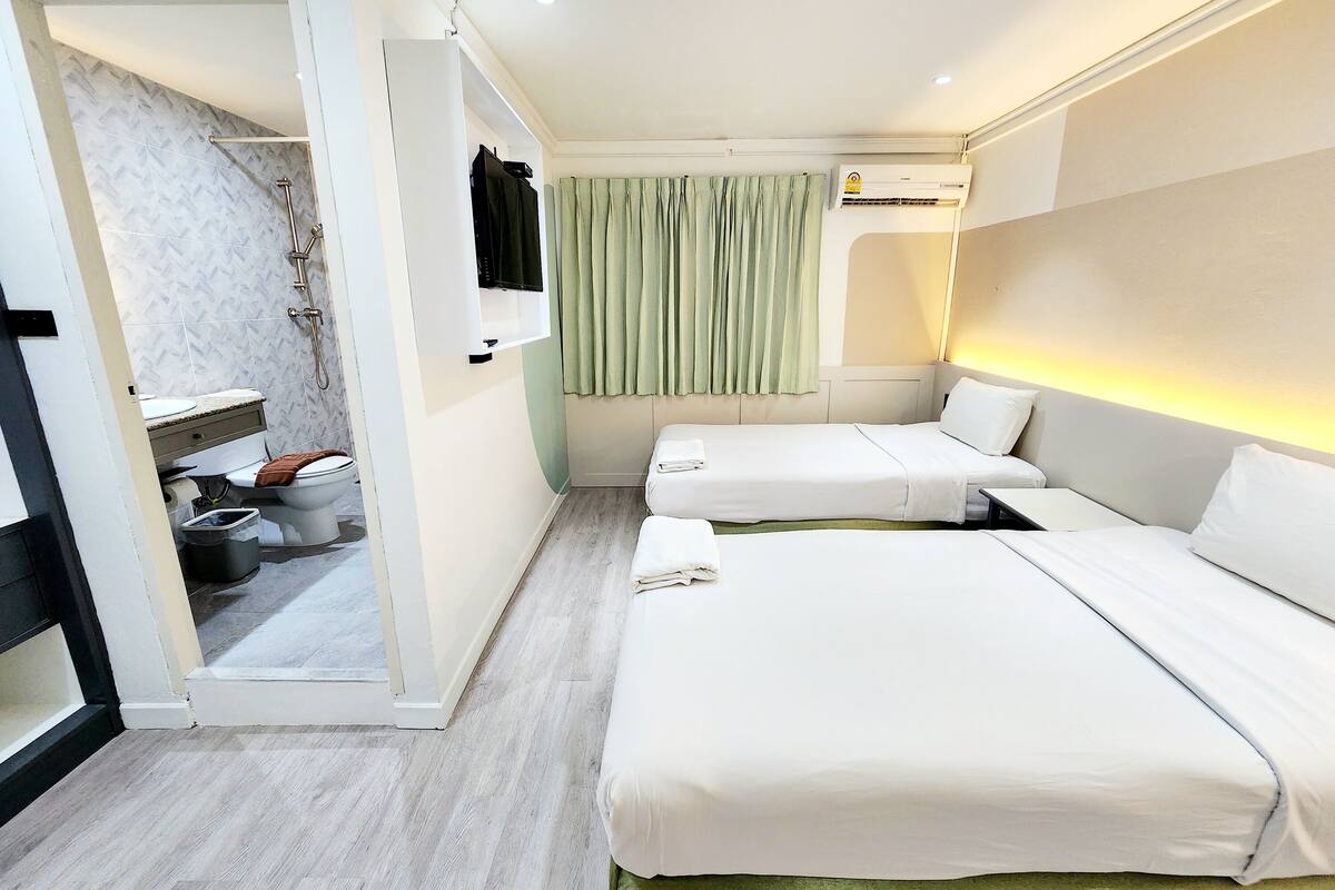 A hotel room with two beds, a bathroom with a shower, and a green curtain.
