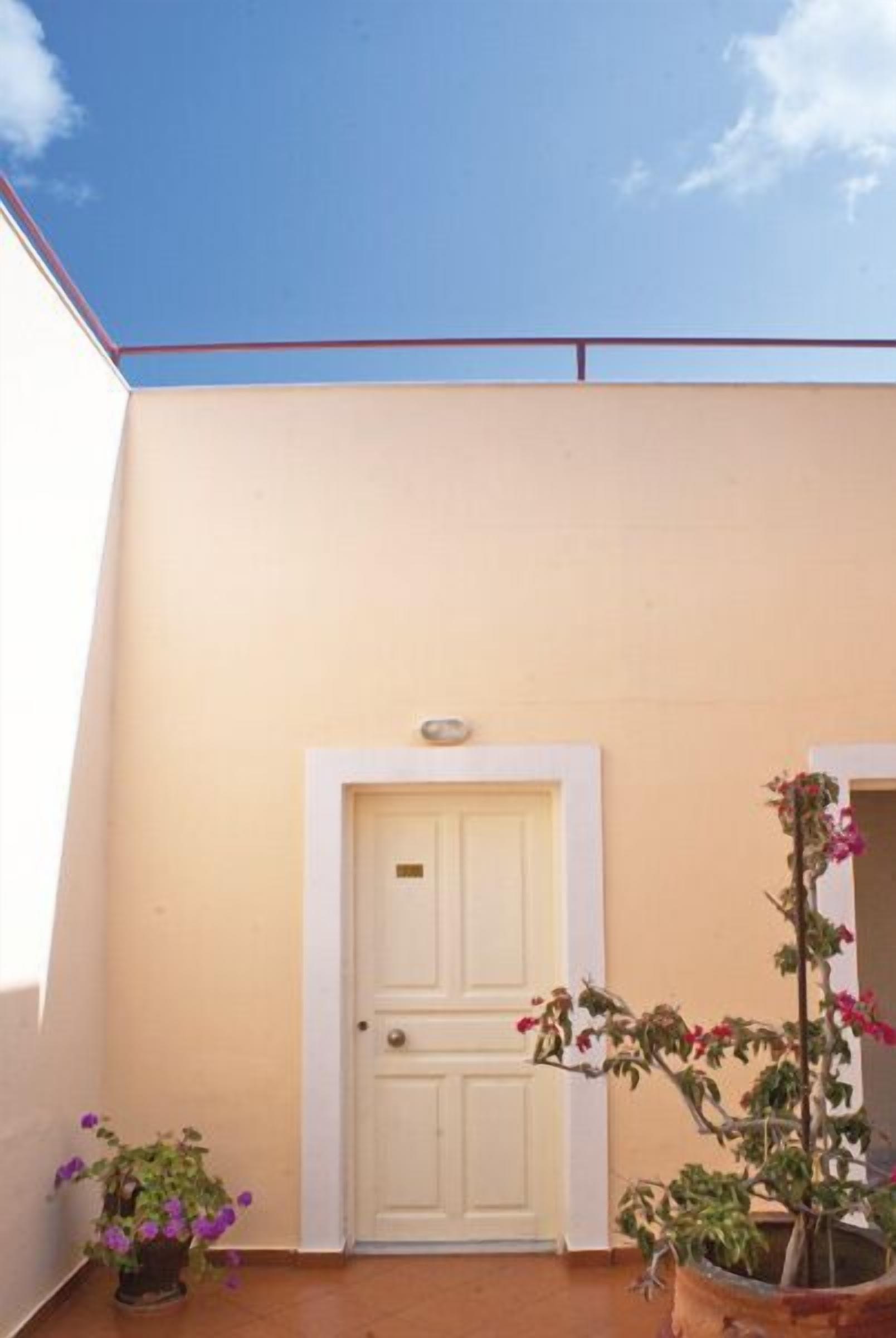 A beige building with a white door and a small balcony with potted plants.
