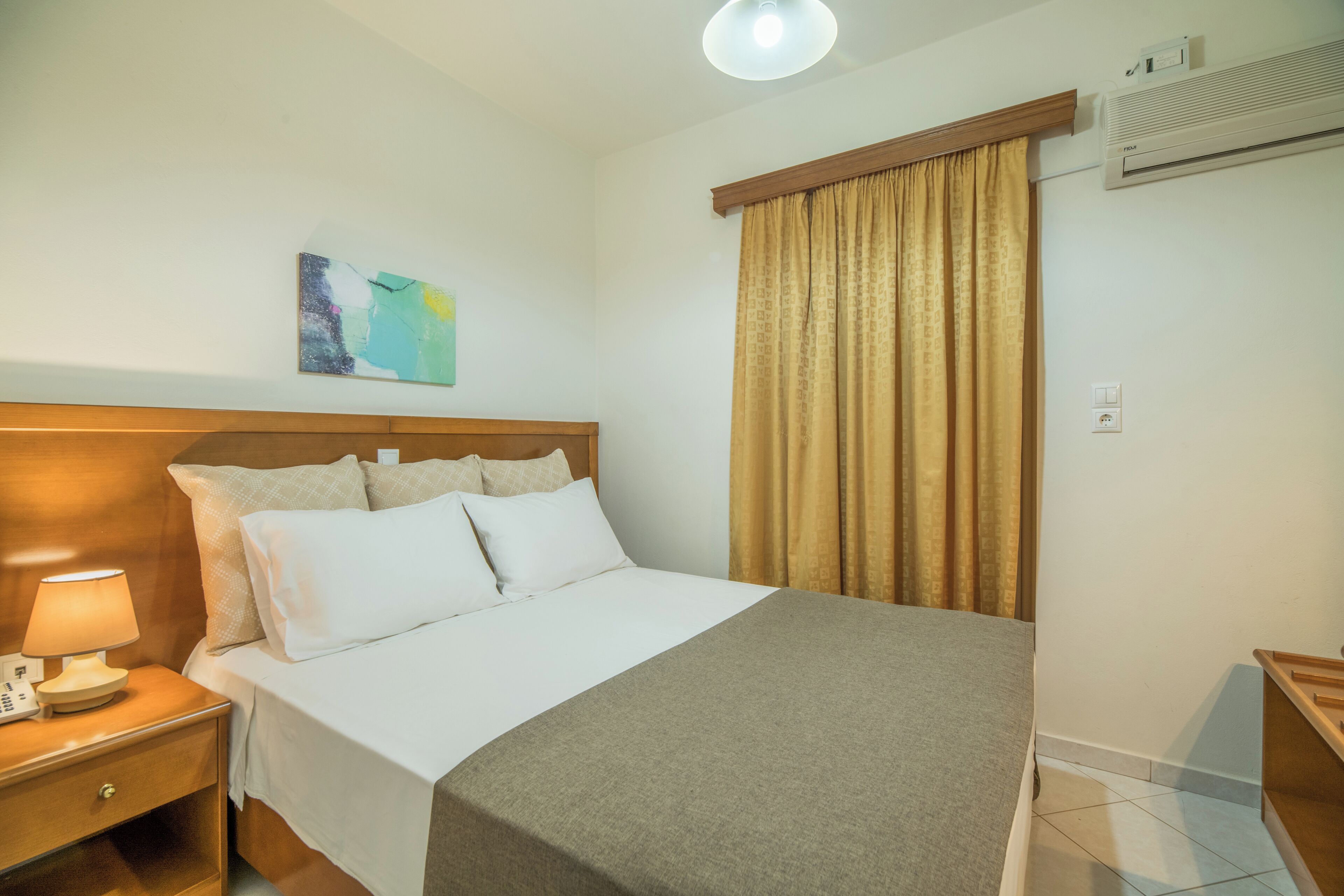 Un lit bien fait, avec une tête de lit, une lampe de chevet et un climatiseur fixé au mur.