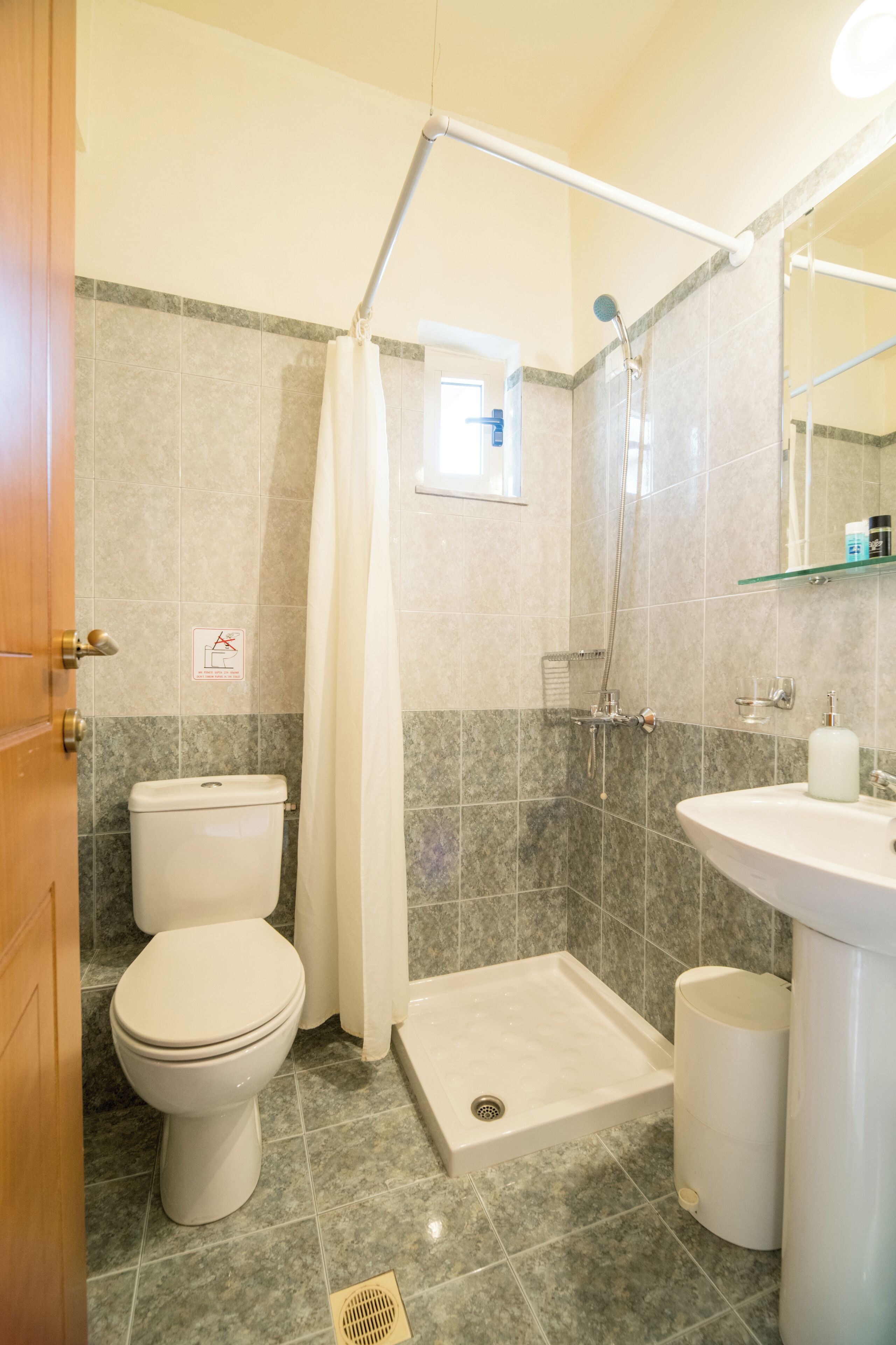 Un baño con inodoro, ducha, lavabo y estante de vidrio.