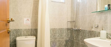 Un baño con inodoro, ducha, lavabo y estante de vidrio.