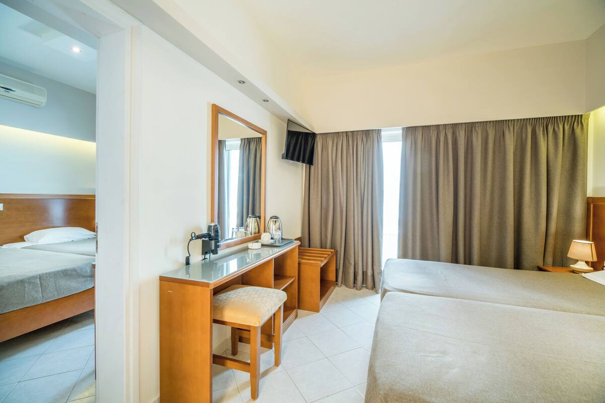 A hotel room with a bed, a desk with a chair, a television, and a window with curtains.