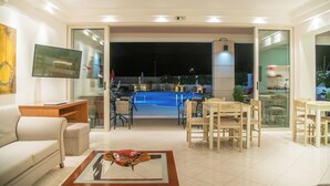 Uma sala de estar moderna com vista para a piscina, televisão de tela plana e área de jantar com mobiliário de madeira.
