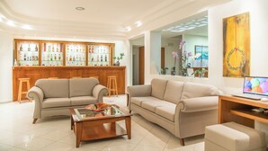 Uma sala de estar ampla, com dois sofás, uma mesa de centro e um balcão de madeira com diversos frascos.